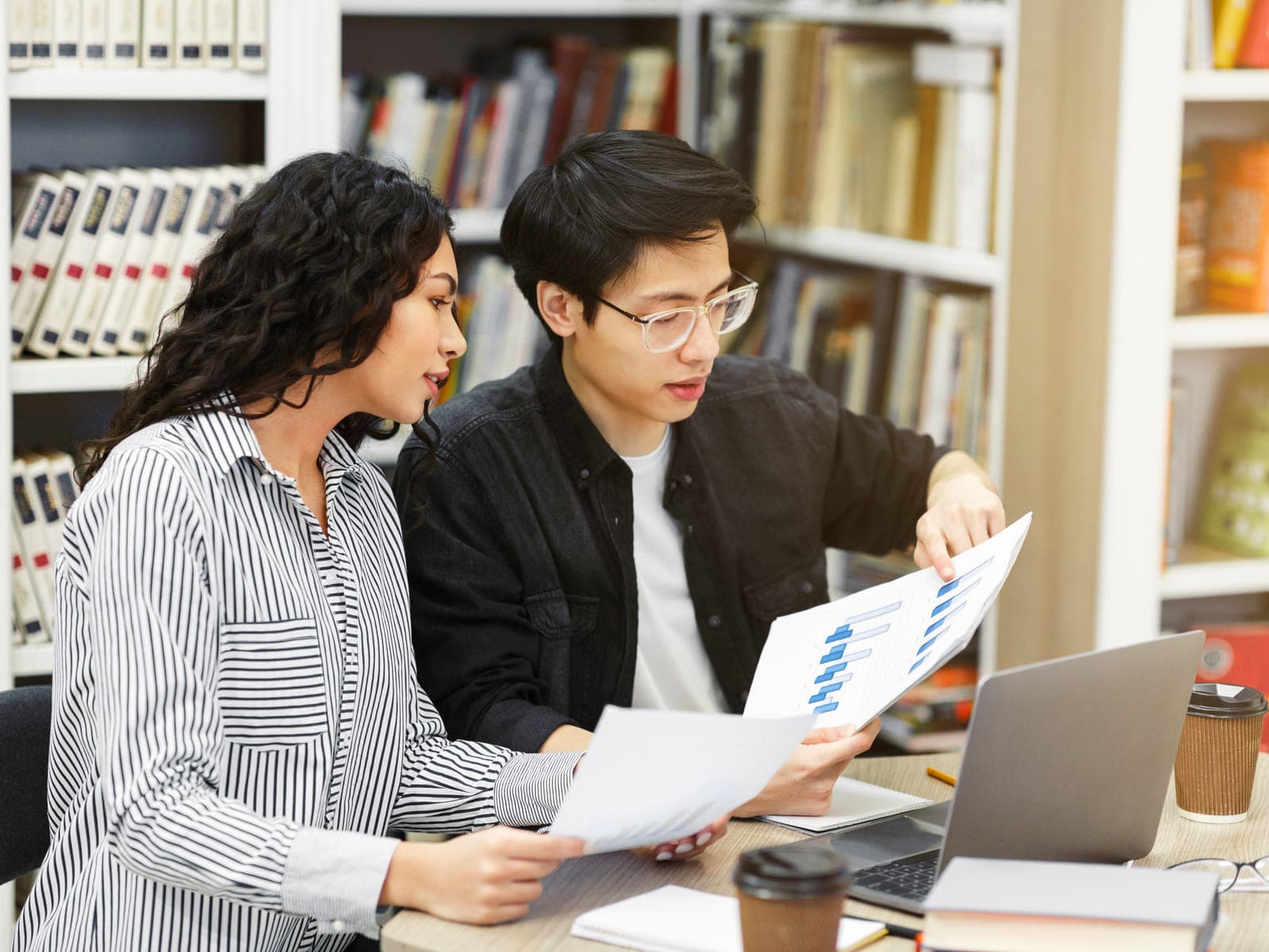 Two people at a desk reviewing printed spec documents together